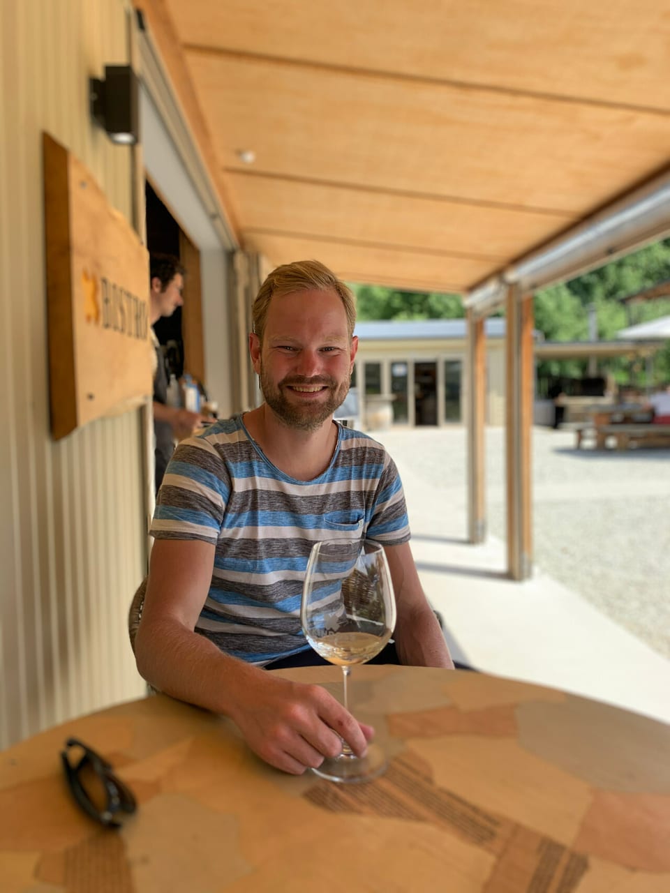 Een glas witte wijn op een houten tafel op een terras, in het zonlicht.